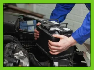Mechanic removing a car battery from an engine compartment during vehicle maintenance.