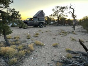 Jeep Gladiator overlanding setup with rooftop tent parked at a remote desert campsite during sunset