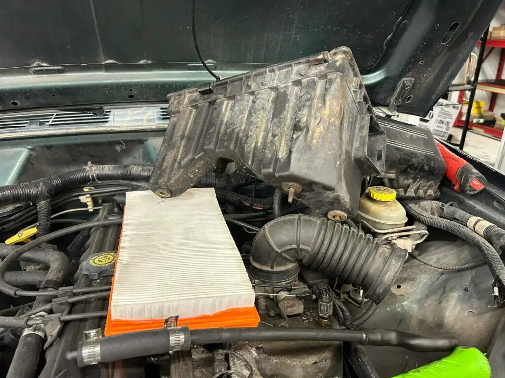 Close-up of a Jeep Wrangler engine compartment with the air filter exposed during a DIY filter replacement.