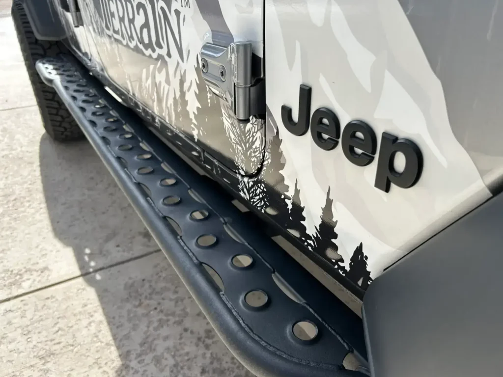 TNT Customs rock sliders installed on a Jeep Gladiator, featuring a durable steel design with a perforated step plate for added grip and protection.