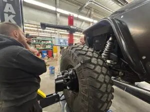 Technicians working on a custom Jeep's wheel alignment using advanced equipment in the shop.