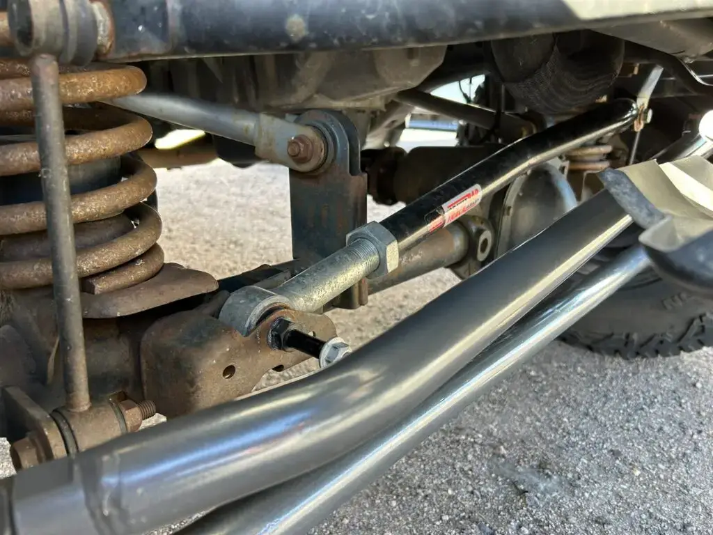 A close-up view of a PSC steering stabilizer mounted on a Jeep’s front axle, with a red differential cover in the background.