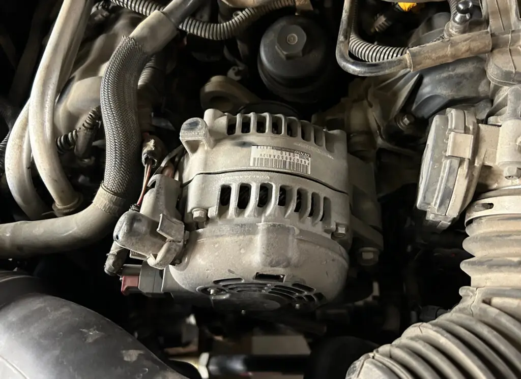 Close-up of an alternator in a vehicle's engine compartment with visible electrical connections.