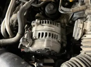 Close-up of an alternator in a vehicle's engine compartment with visible electrical connections.