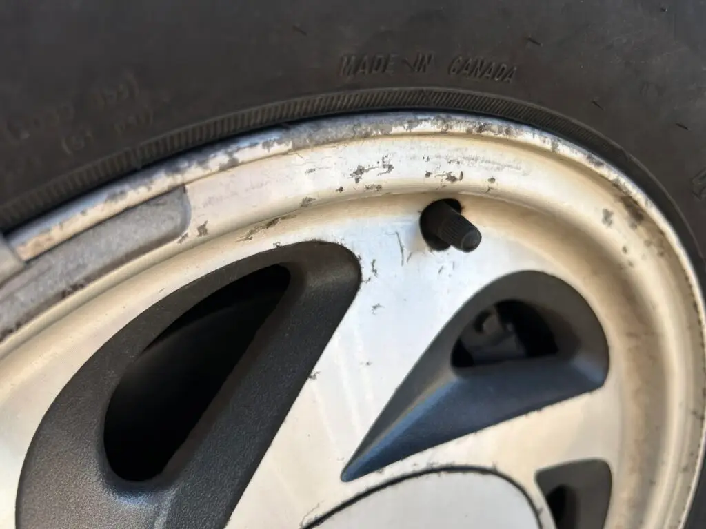 Close-up photo of an aluminum alloy wheel with paint chipping around the rim and a visible valve stem.