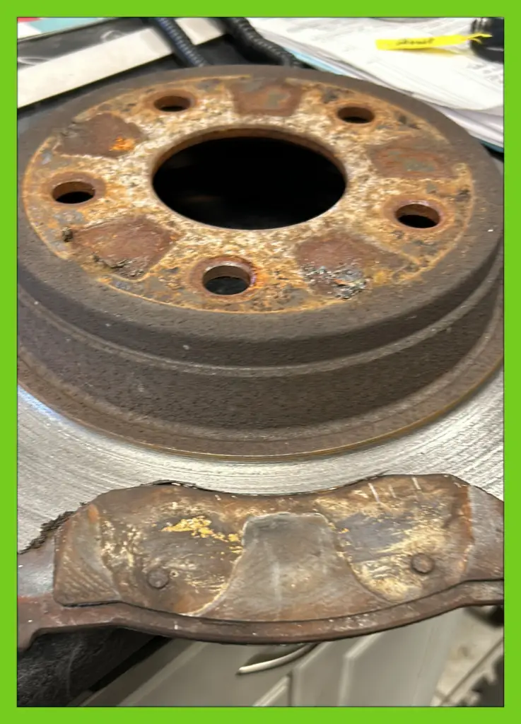 Rusty brake drum and worn-out brake shoe on a workbench during a vehicle brake service.