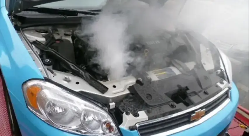 Blue Chevrolet car with hood open and thick steam rising from the engine due to overheating.
