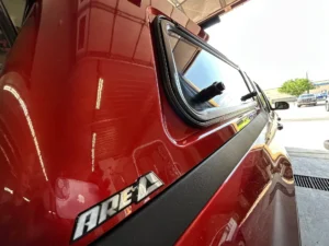 Close-up side view of a red truck with a glossy ARE topper installed, highlighting the reflective window and ARE logo.