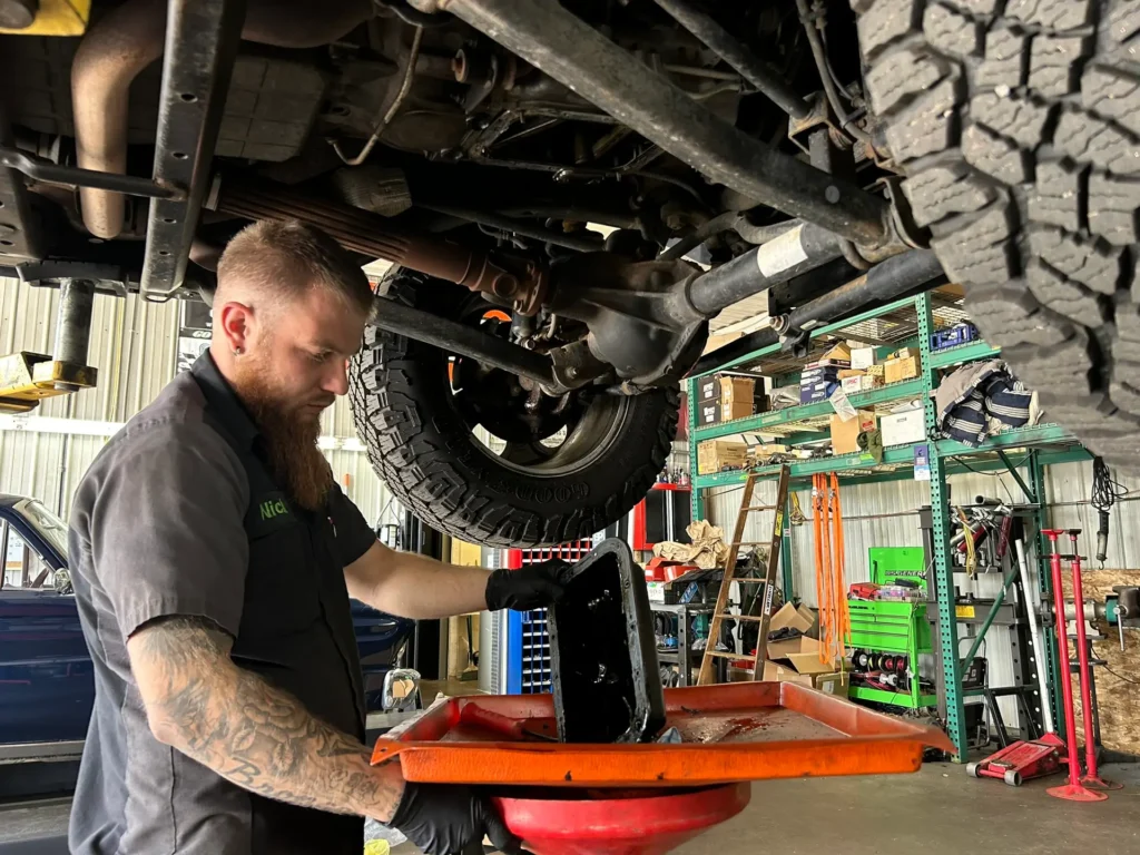 Auto technician draining fluid during a vehicle service at TNT Customs auto shop