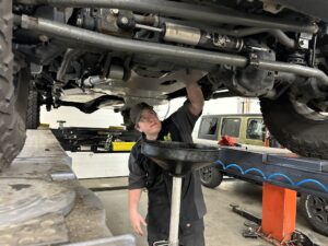 Mechanic from TNT Customs drains oil from a lifted Jeep on a shop lift.