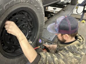 Technician checking and adjusting tire pressure on a vehicle wheel using a digital tire gauge inside the TNT Customs auto shop.