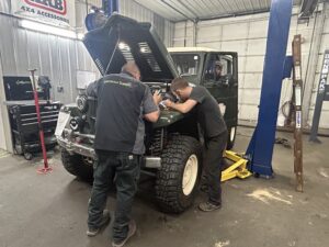 TNT Customs technicians diagnosing and working on a green Jeep inside the TNT Customs auto repair shop in Cheyenne, Wyoming.