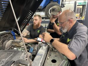 Close-up of TNT Customs technicians inspecting the engine bay of a vintage Jeep during diagnostics and repair work in Cheyenne, Wyoming.