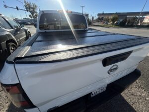 White Nissan Frontier with a hard folding tonneau cover professionally installed by TNT Customs in Cheyenne, Wyoming.
