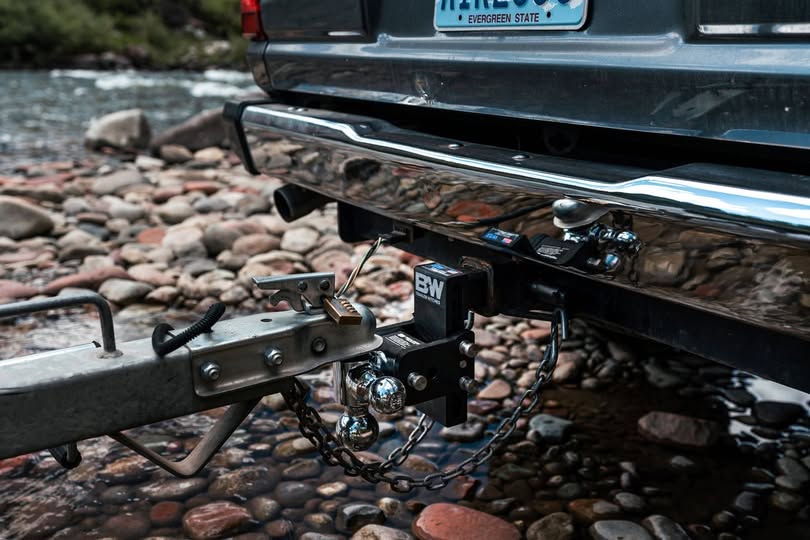 Close-up of a B&W adjustable trailer hitch with safety chains and trailer coupler connected to a pickup truck.