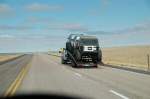 Pickup truck safely towing multiple Jeep Wranglers on a car hauler trailer along an open Wyoming highway.